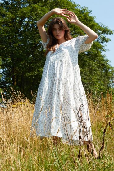 a woman wearing a white dress, standing in long dry grass in the summer sun